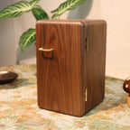 Wooden box with a gold handle on a decorative surface with plants and a lamp in the background