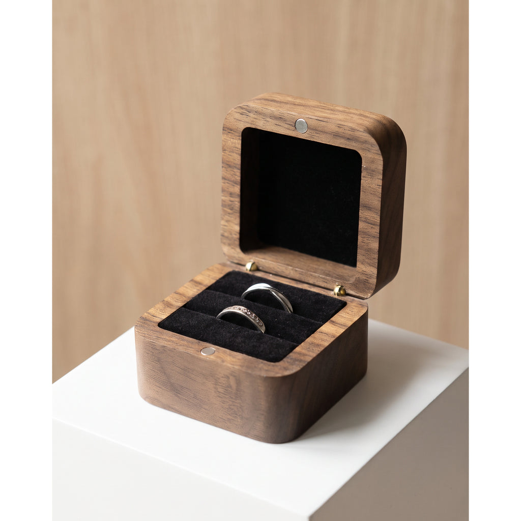 Walnut wood ring box with open lid and black velvet cushion holding two rings